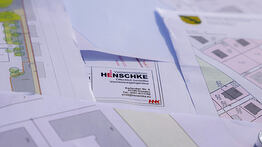 Eine Hand hält eine messingfarbene Grenzmarke mit der Aufschrift „Grenzpunkt“ über einem Fach im Werkzeugkasten, in dem weitere Kunststoffhülsen und Arbeitsmaterialien liegen