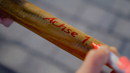 Eine Hand beschriftet einen Holzpflock mit der Aufschrift „Achse 1.“ zur Markierung für eine Bauvermessung