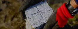 Nahaufnahme eines Granit-Grenzsteins mit Kreuzmarkierung, der mit Handschuhen in Position gebracht wird