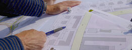 Vermessungsingenieuer aus Dresden zeigt mit einem Kugelschreiber auf einen Plan mit Gebäuden und Grundstücksgrenzen