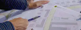 Vermessungsingenieuer aus Dresden zeigt mit einem Kugelschreiber auf einen Plan mit Gebäuden und Grundstücksgrenzen