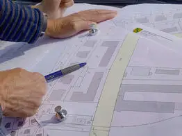 Vermessungsingenieuer aus Dresden zeigt mit einem Kugelschreiber auf einen Plan mit Gebäuden und Grundstücksgrenzen