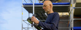 Vermessungsingenieur Andreas Henschke führt mit einem GPS-Messgerät Vermessungsarbeiten auf einer Baustelle mit Gerüst durch