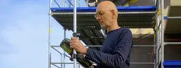 Vermessungsingenieur Andreas Henschke führt mit einem GPS-Messgerät Vermessungsarbeiten auf einer Baustelle mit Gerüst durch