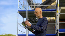 Vermessungsingenieur Andreas Henschke führt mit einem GPS-Messgerät Vermessungsarbeiten auf einer Baustelle mit Gerüst durch