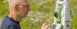 Vermessungsingenieur Andreas Henschke verwendet eine Leica TS15 Totalstation auf einer Blumenwiese bei sonnigem Wetter