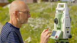 Vermessungsingenieur Andreas Henschke verwendet eine Leica TS15 Totalstation auf einer Blumenwiese bei sonnigem Wetter