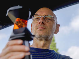 Ein Vermessungsingenieur betrachtet konzentriert einen Prisma-Reflektor bei blauem Himmel über ihm