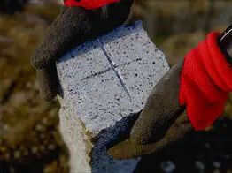 Nahaufnahme eines Granit-Grenzsteins mit Kreuzmarkierung, der mit Handschuhen in Position gebracht wird